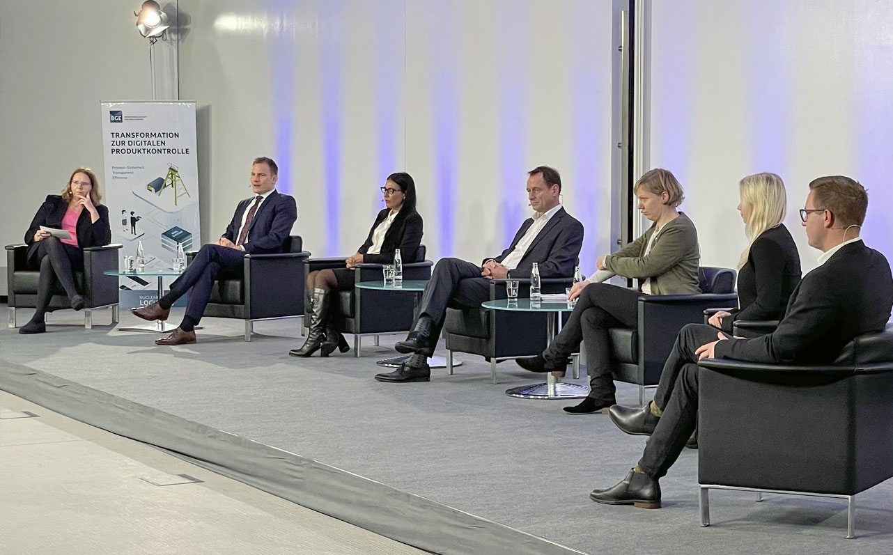 Video-Konferenz zur Vorstellung des Pilotsystems Menschen sitzen in Sesseln auf der Bühne